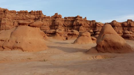 Gorgeous-dolly-in-aerial-drone-shot-of-the-beautiful-Goblin-Valley-Utah-State-Park-approaching-strange-mushroom-rock-formations-with-red-hoodoo-formations-in-the-background-on-a-warm-sunny-summer-day