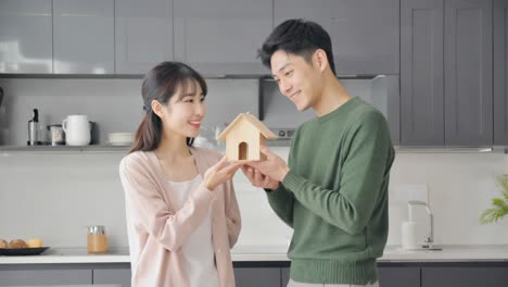 happy couple in kitchen holding model house