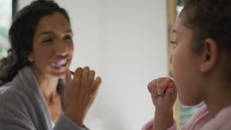 happy mixed race mother and daughter brushing teeth in bathroom