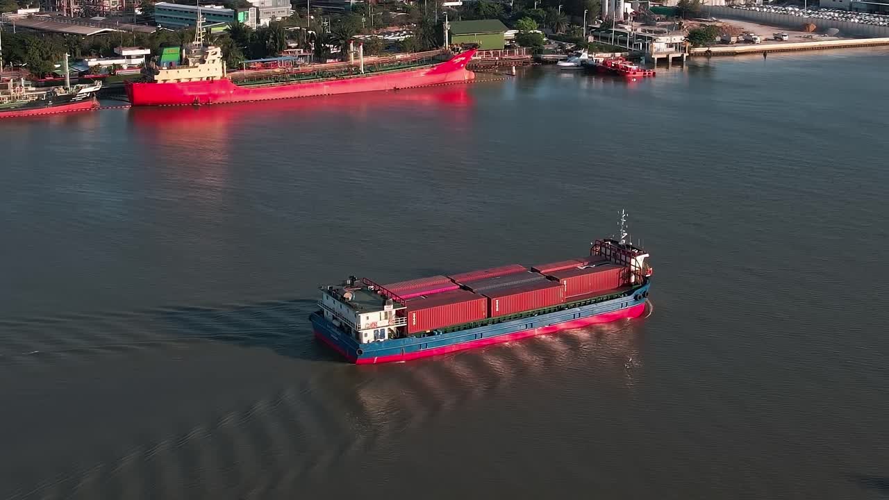 Cargo ship navigates river in Bangkok at sunset with city skyline nearby