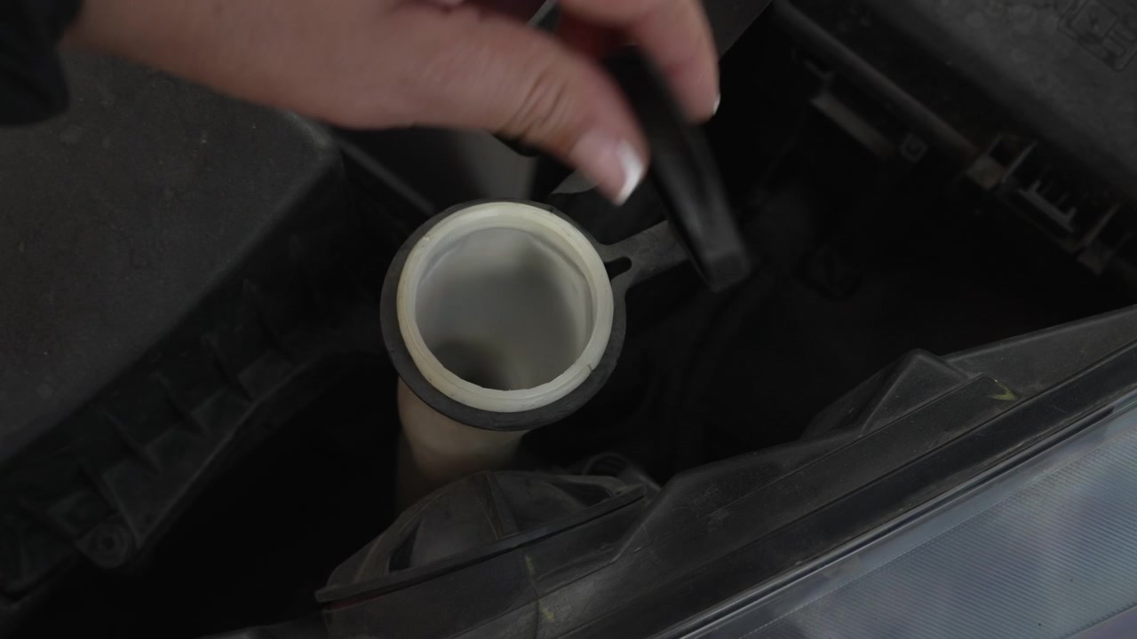 Female hand opening the windscreen washer fluid cap under the hood of a modern automobile