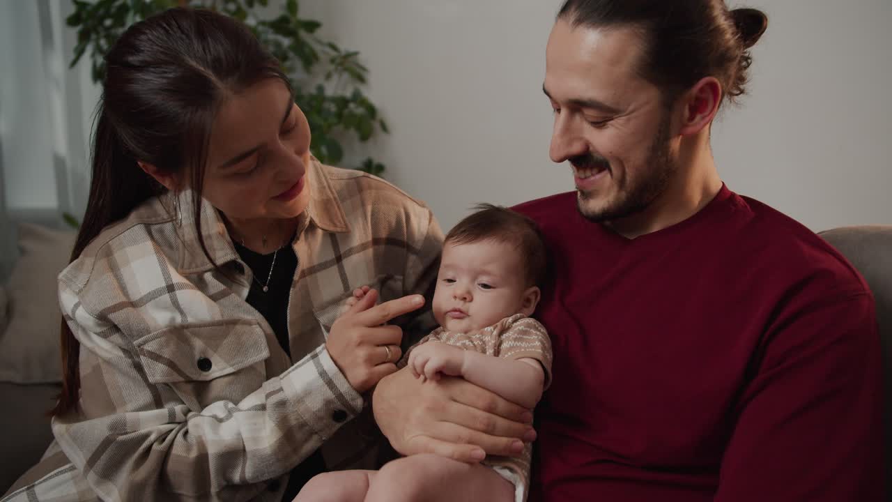 primer plano de una madre feliz en una camisa a cuadros juega con su pequeña hija bebé mientras ella es sostenida por su padre en un apartamento moderno. padres felices jugando con su hija en un departamento moderno