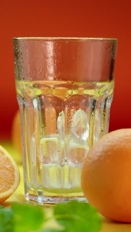 refreshing drink concept with empty glass and ice cubes dropping, surrounded by fresh oranges and mint