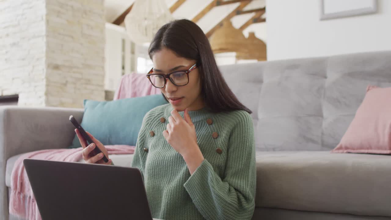 mujer biracial usando computadora portátil y sonriendo en la sala de estar