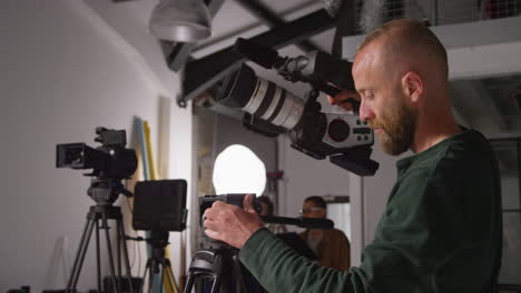 male film camera operator taking camera off tripod to shoot handheld movie or video in studio