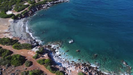 Shore-of-Crete-Island-with-waves-hitting-the-beach-surrounded-by-forest-and-trails