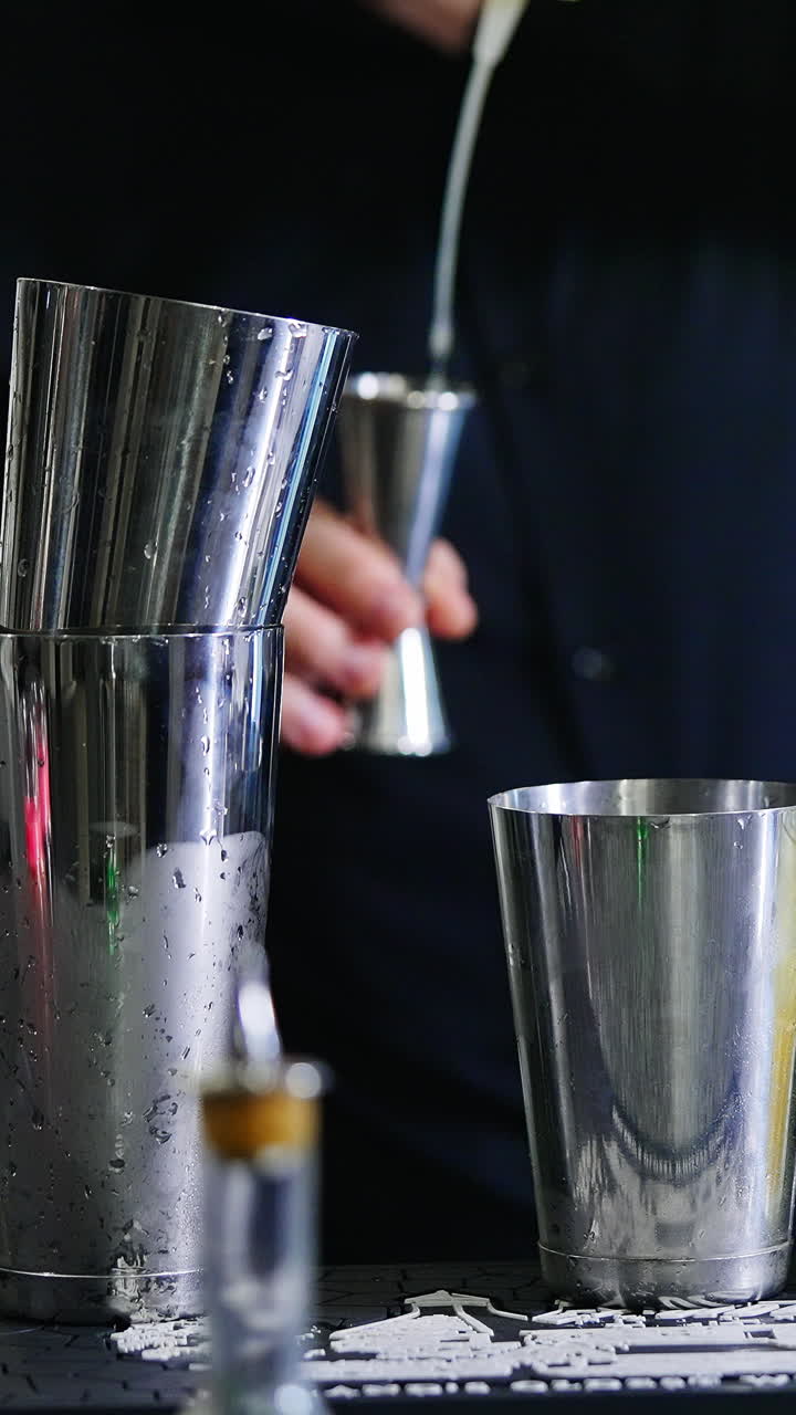 Bartender at working place at bar stand. Male barman preparing cocktails using metal glasses. Close up. Blurred backdrop. Vertical video