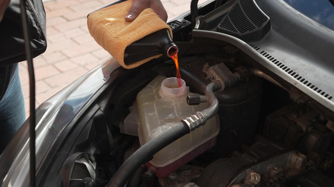 Professional mechanic pouring red coolant into the car's cooling system reservoir for maintenance