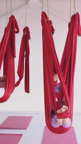 relaxed ladies group lie and rest in big red aerial fly yoga hammocks in spacious white room for pilates