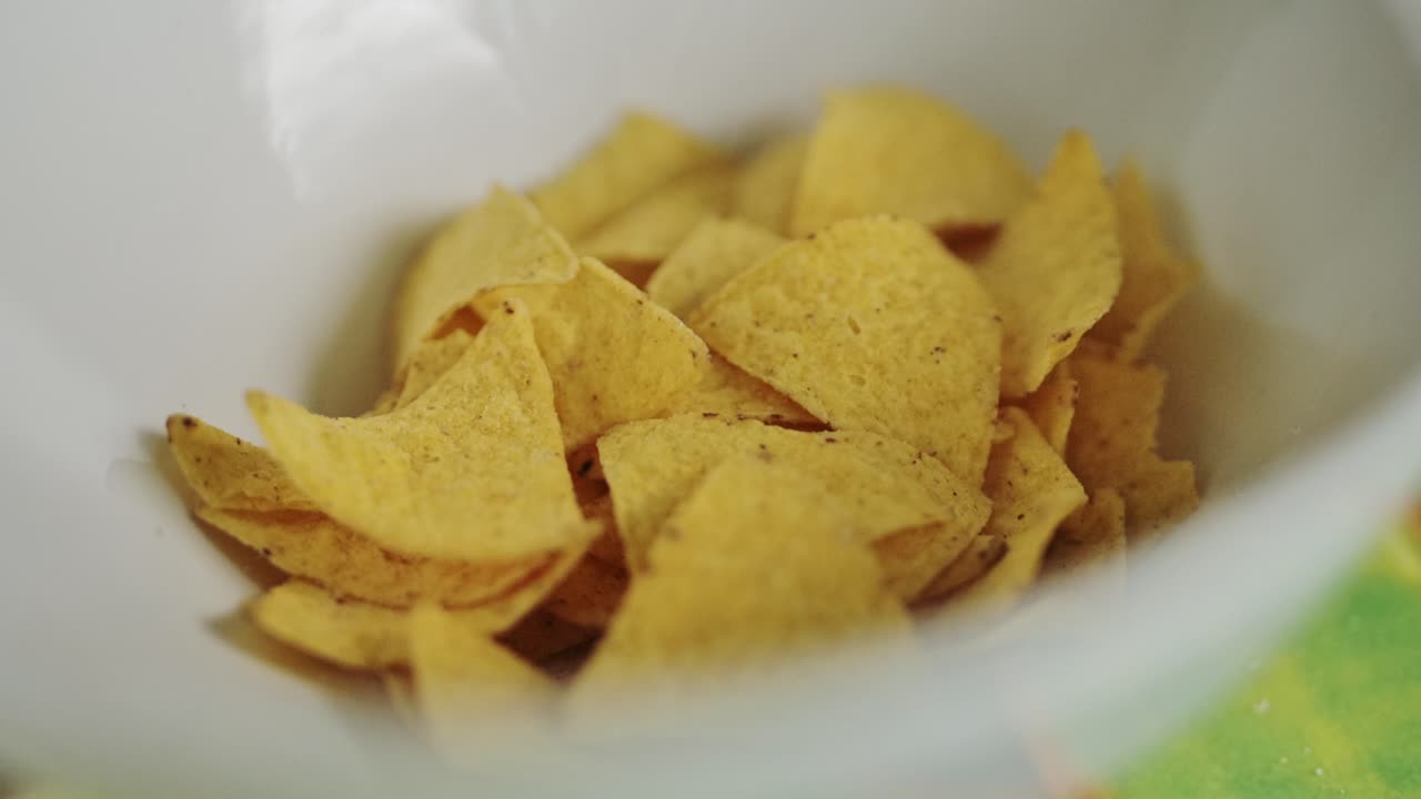 Handheld close up shot of yellow tortilla chips falling into white bowl, Snacks