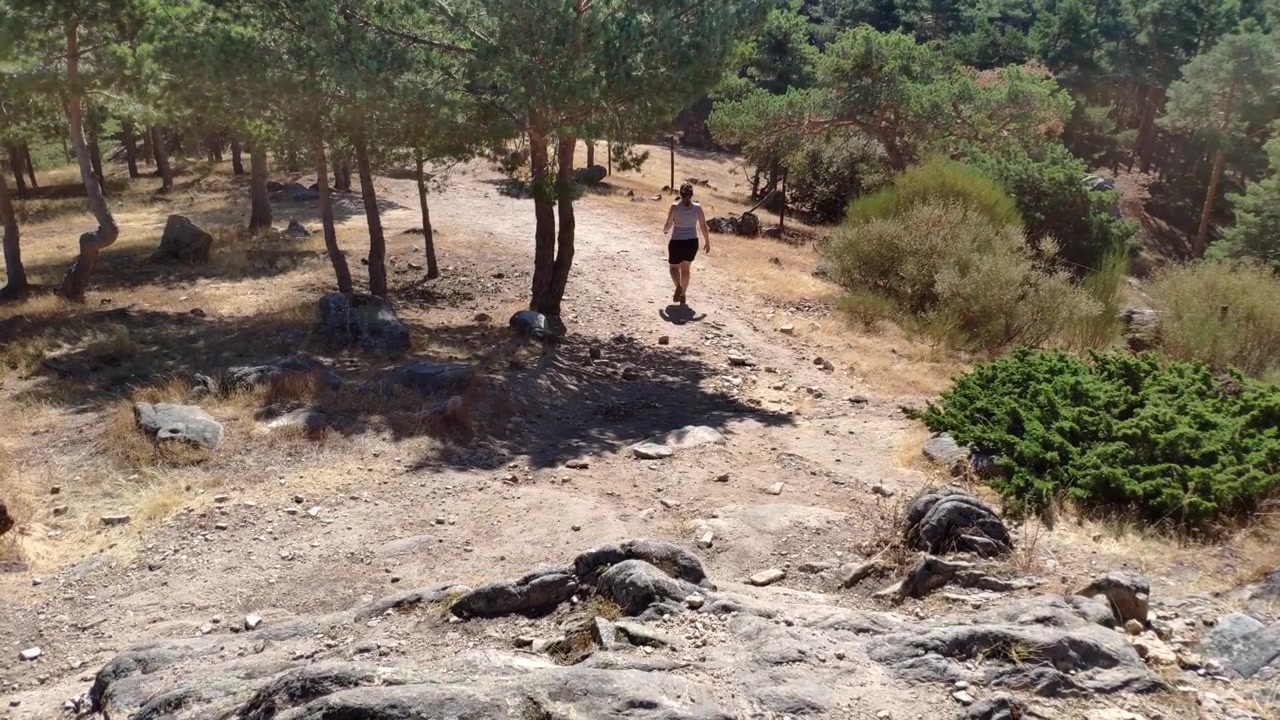 Mulher fazendo trilha em uma trilha florestal seca e rochosa sob luz diurna intensa