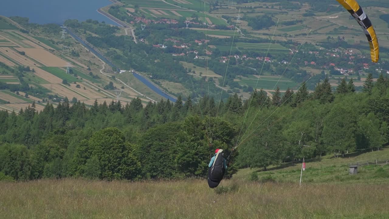 A man takes off for his paragliding adventure, gliding just above the ground before gaining altitude over the forest