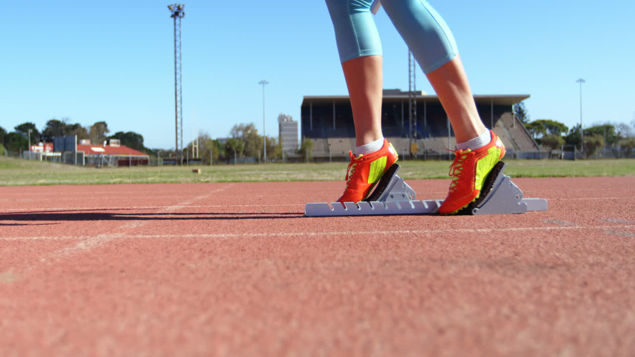 sección baja de una atleta femenina tomando la posición de salida en una pista de atletismo