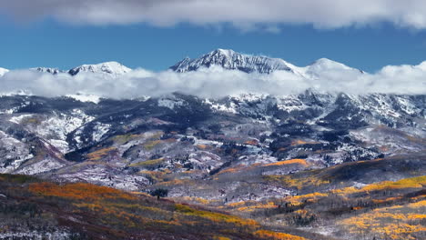 kebler pass aerial cinematic drone crested butte gunnison colorado seasons collide early fall aspen tree red yellow orange forest winter first snow powder rocky mountain peak clouds circle left motion