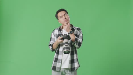 asian photographer thinking about the pictures footage and raising his index finger while looking at the pictures in the camera on green screen background in the studio