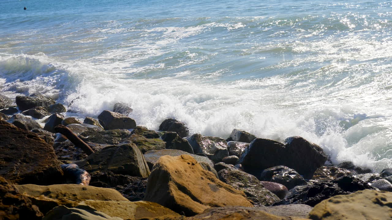 una gran ola oceánica chocando y en cámara lenta contra una playa rocosa de california y rociando agua blanca en el aire