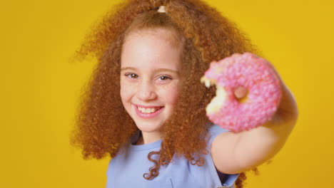 studio portrait of girl eating donut against yellow background