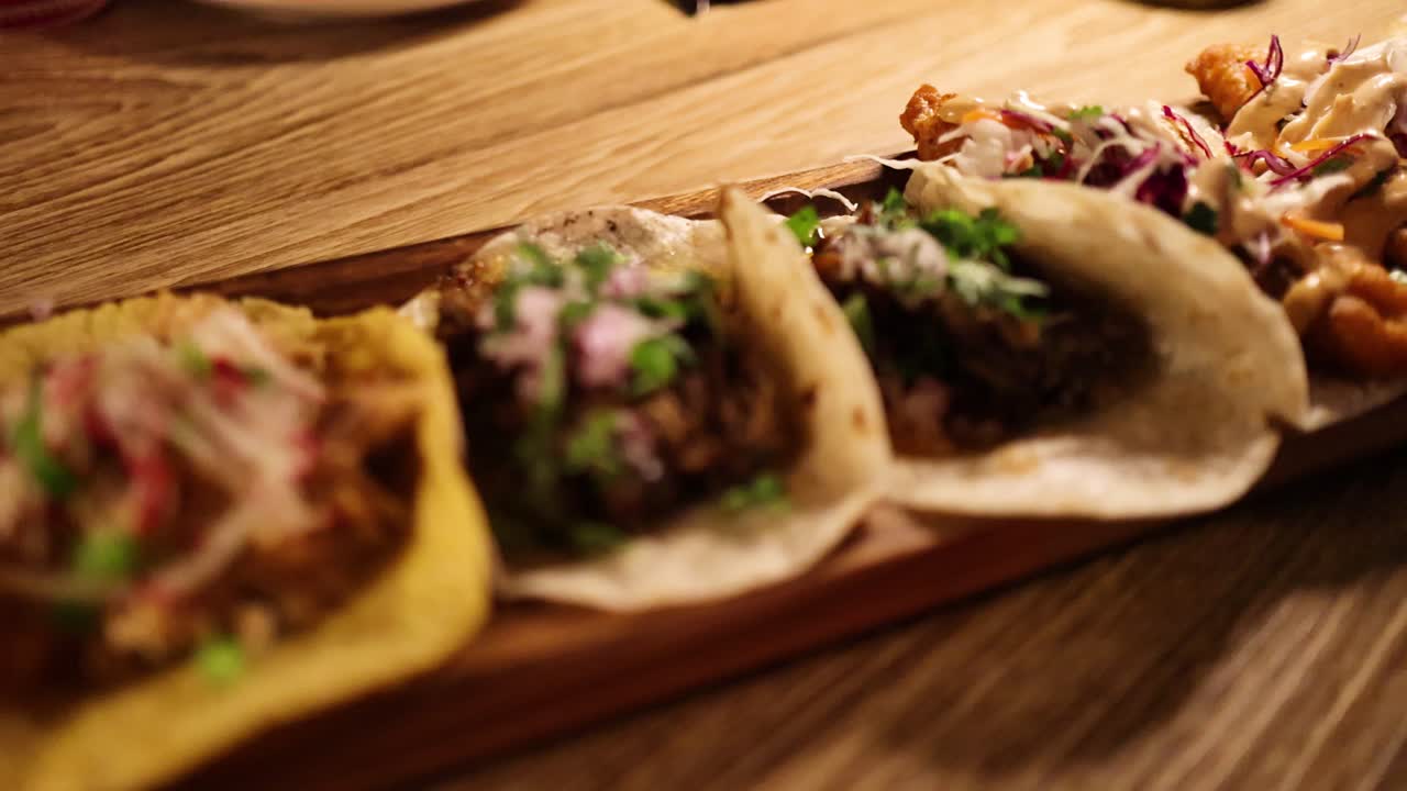 Close-up of assorted tacos on a wooden platter in warm lighting at a Bangkok restaurant