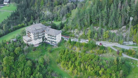 drone view of a building on a hill with trees and mountains surround it