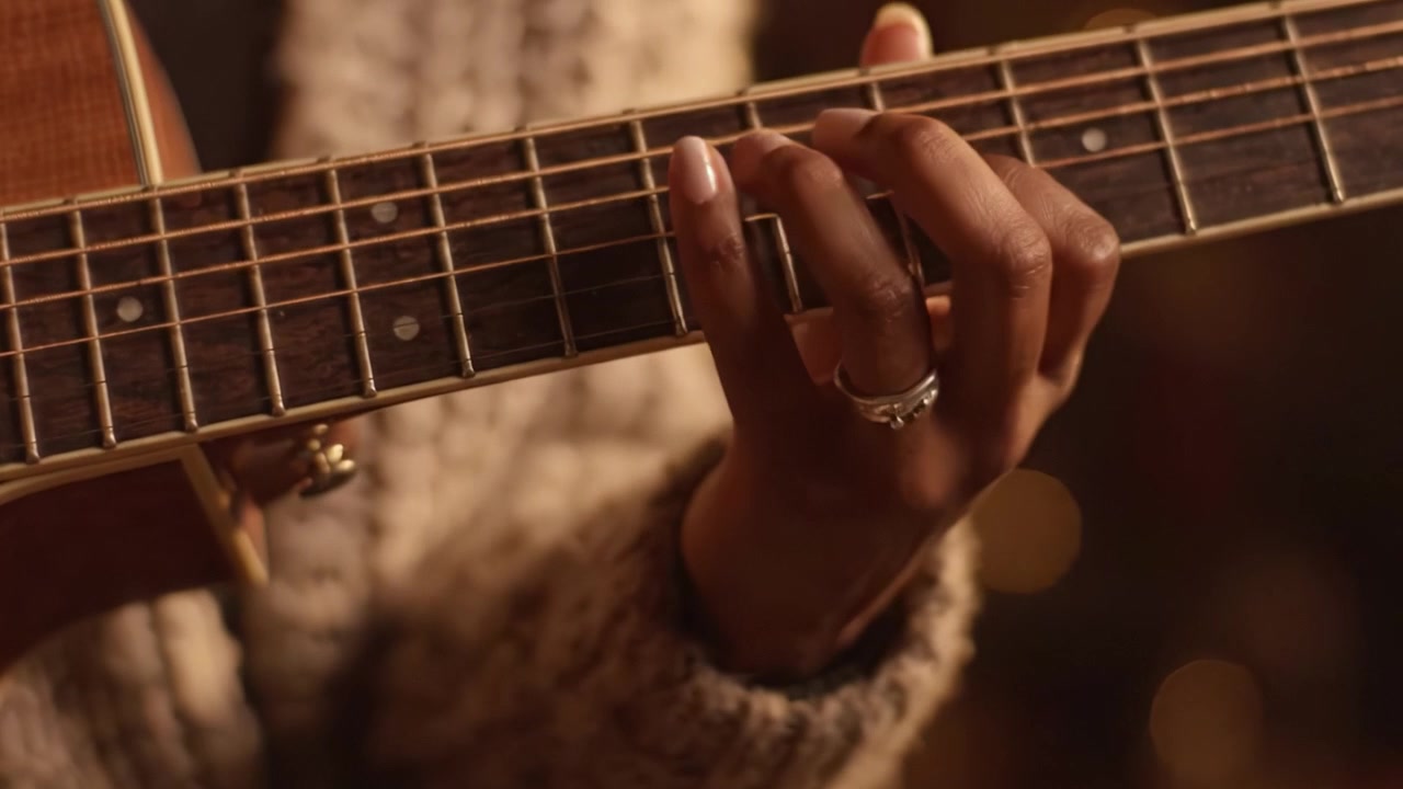 Un primo piano della mano di un individuo che strimpella abilmente una chitarra acustica, catturando l'essenza della musica e della passione in un'atmosfera accogliente