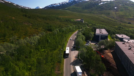 Vehicles-Driving-On-Mountain-Road-Passing-By-Apartment-Buildings-In-Tromso,-Northern-Norway