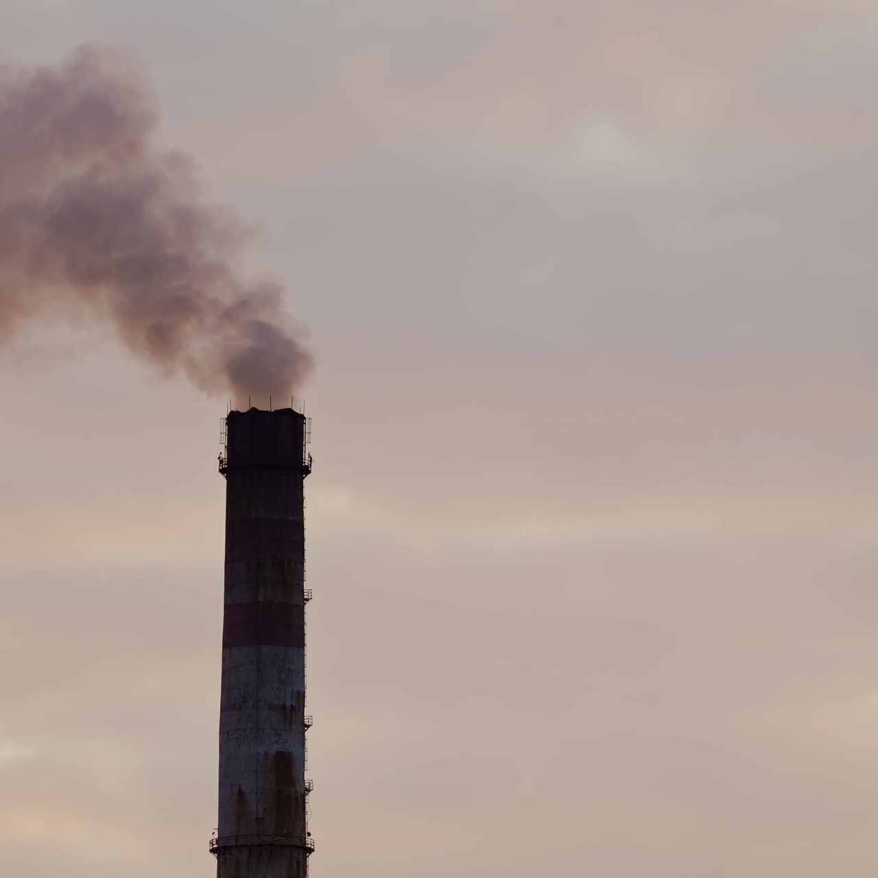 Dark factory against the orange setting sun. Factory pipes with smoke. Dirty smoke pours out of chimneys into the air on the river background. Aerial view video