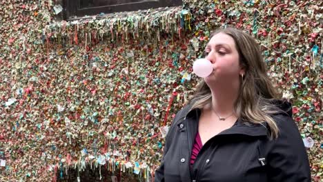 woman blowing bubble gum ball beside colourful gum wall under pike place market in downtown seattle