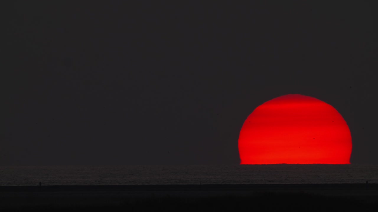 lapso de tiempo de la bola de fuego solar durante el hundimiento de la puesta de sol en el agua del mar del océano, planeta estrella roja en el cielo oscuro, concepto de calentamiento del cambio climático