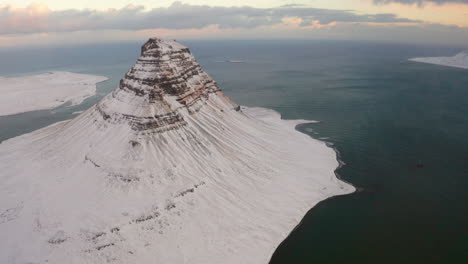 cinematic shot of massive kirkjufell mountain snow-covered and cold fjord water in background during winter day