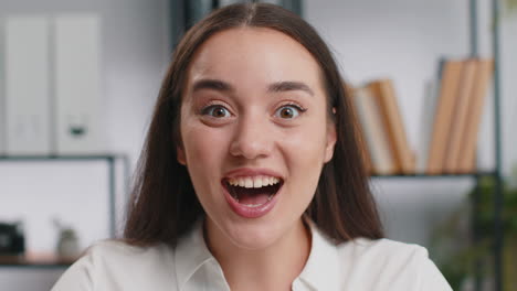 business woman working at home office taking off glasses shocked by sudden victory lottery winning