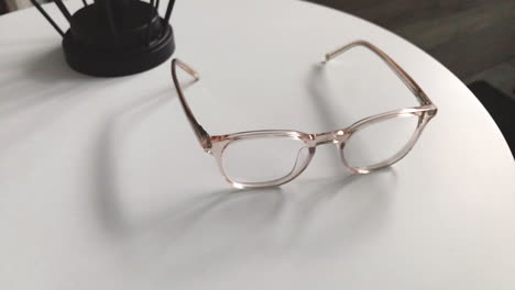 modern eyeglasses in light colour lie on a white table, bright glasses frame, slow motion footage