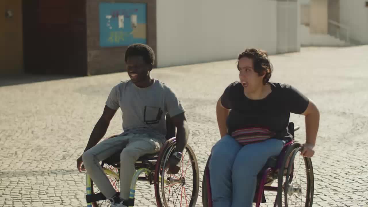 Casal jovem feliz passeando pela rua em cadeiras de rodas