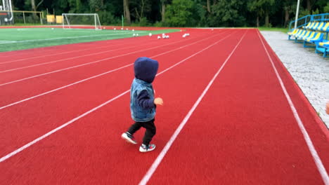 rear view of mom and son walking by the stadium. little active toddler runs by the track.