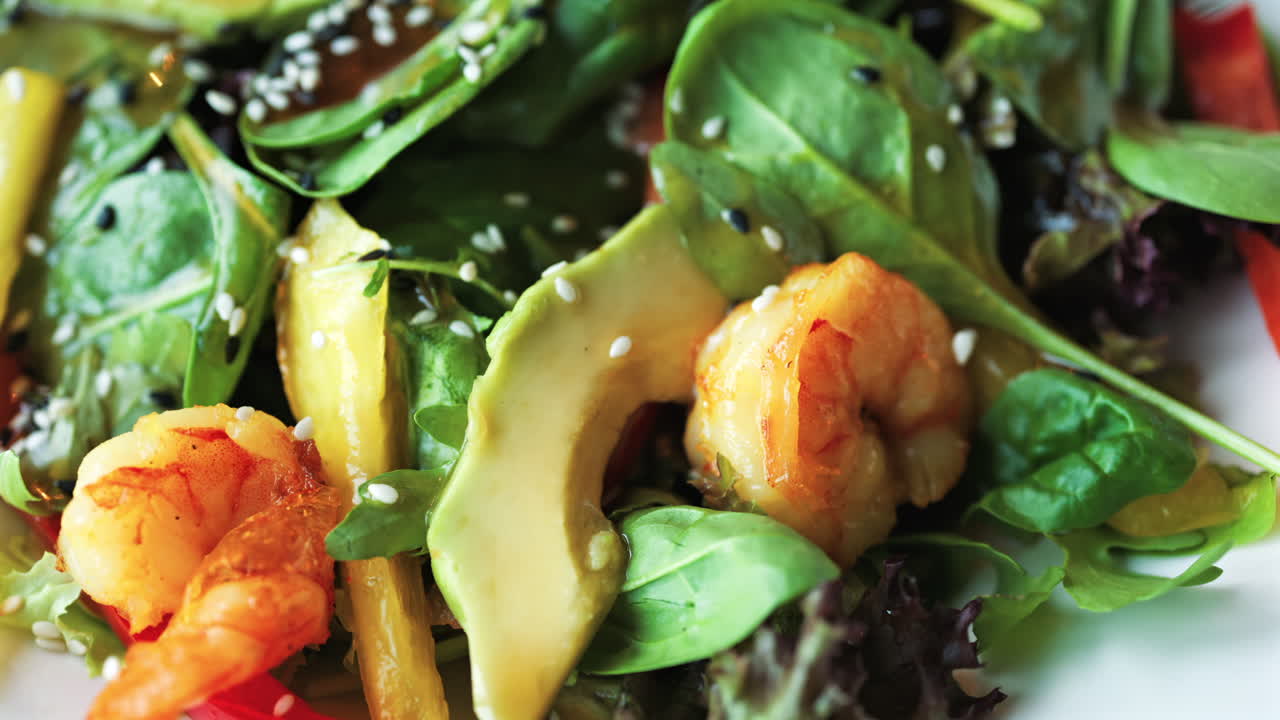 Close up of a salad with spinach, avocado, shrimp, and peppers on a white plate