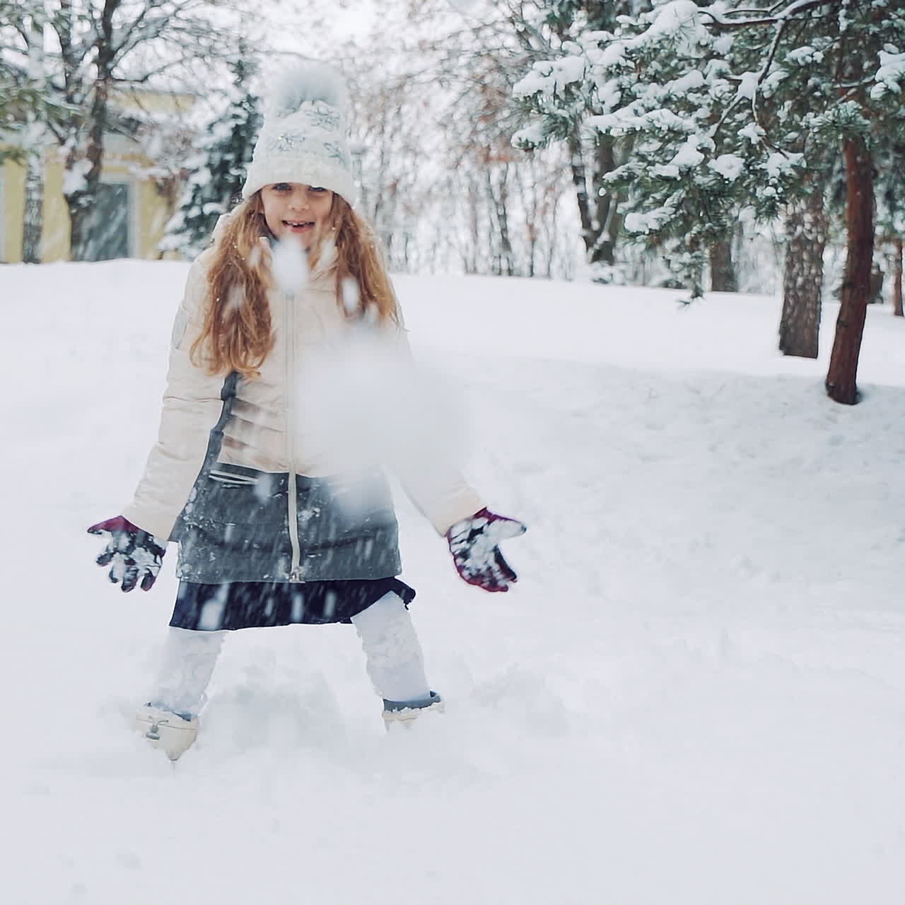 Pretty girl is playing with snow in the park in winter. Active kid throws up white snow and has a lot of fun with it outdoors. Slow motion.