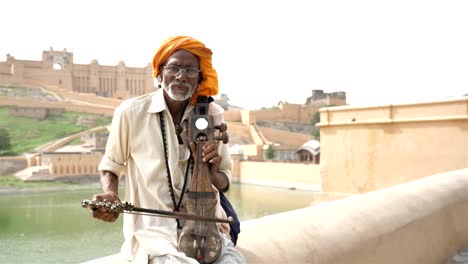 an old traditional man playing sarangi against the historic fort.