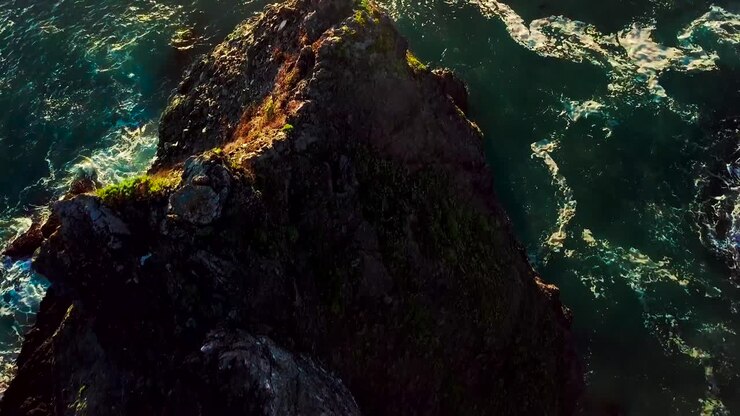 Vista aerea al tramonto di onde verdi dell'oceano che si infrangono contro scogliere rocciose a Big Sur, California
