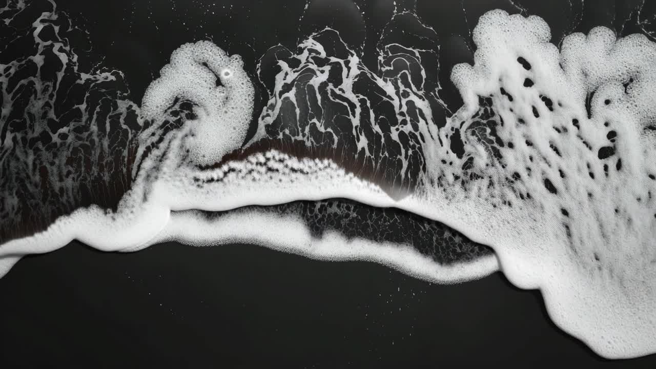 Aerial view of ocean waves creating intricate patterns on a black sand beach