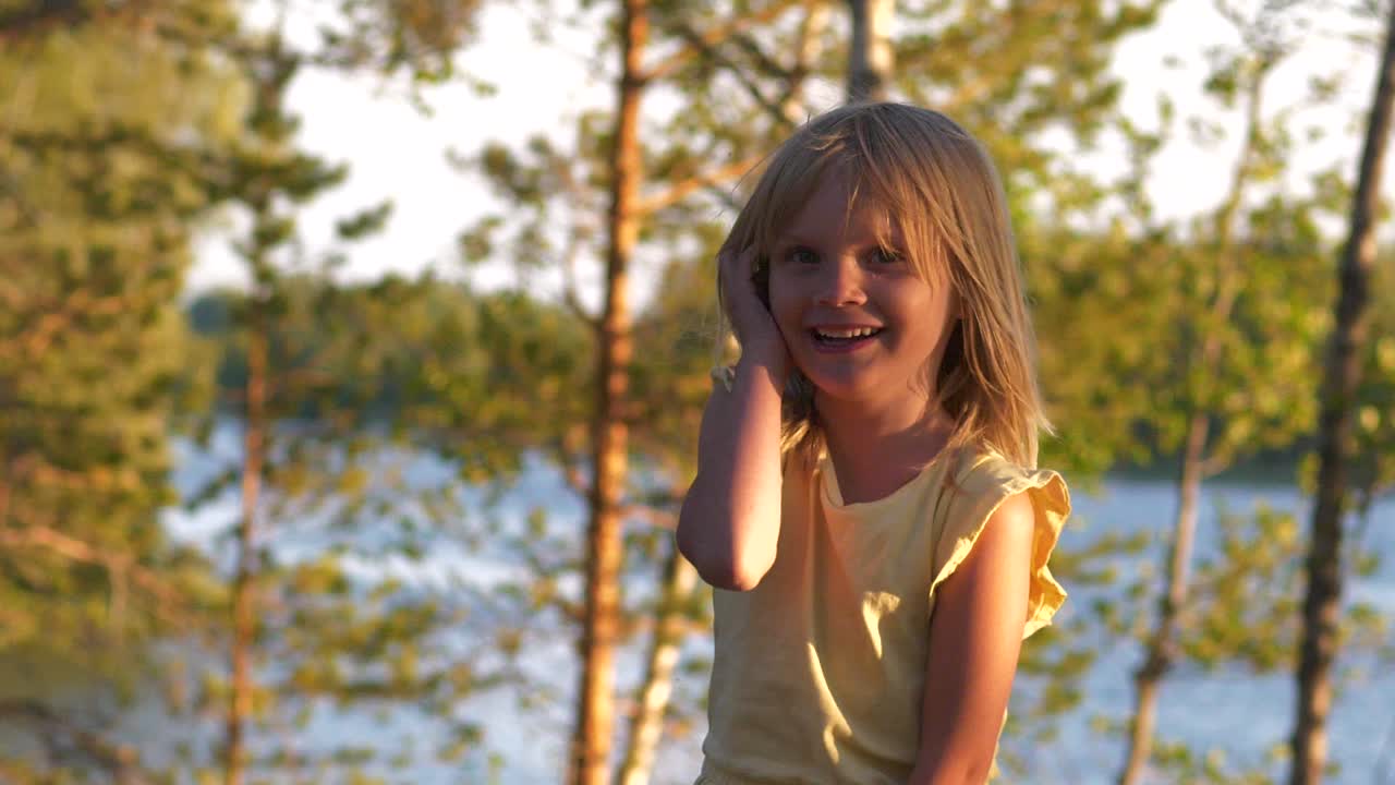 Uma jovem garota loira pula e ri feliz, com lago ao fundo ao pôr do sol