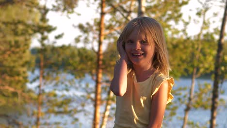 a young blonde girl happily jump and laugh, lake background at sunset