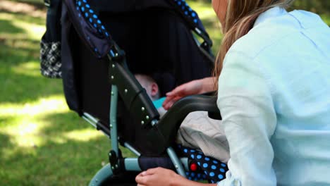 mother checking on her sleeping baby in a pram in the park