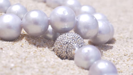 cinematic close up of a natural pearl necklace with silver jewellery laying on a sandy beach, 120 fps, slomo