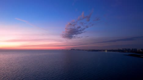 single puffy cloud flouting over sea with bright pink sunrise and city skyline