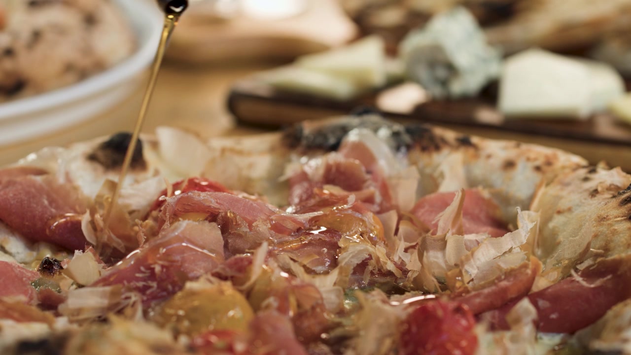 Primo piano di olio d'oliva dorato versato a filo su pizza artigianale cotta nel forno a legna in un ristorante.