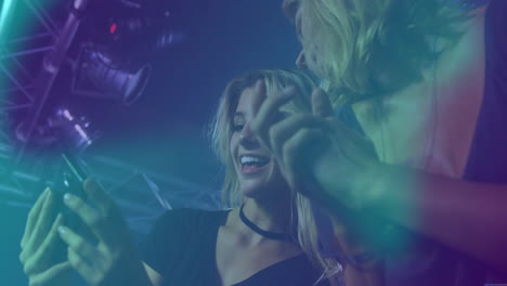two women comparing marketing app screen in nightclub, showing animated neon music notes