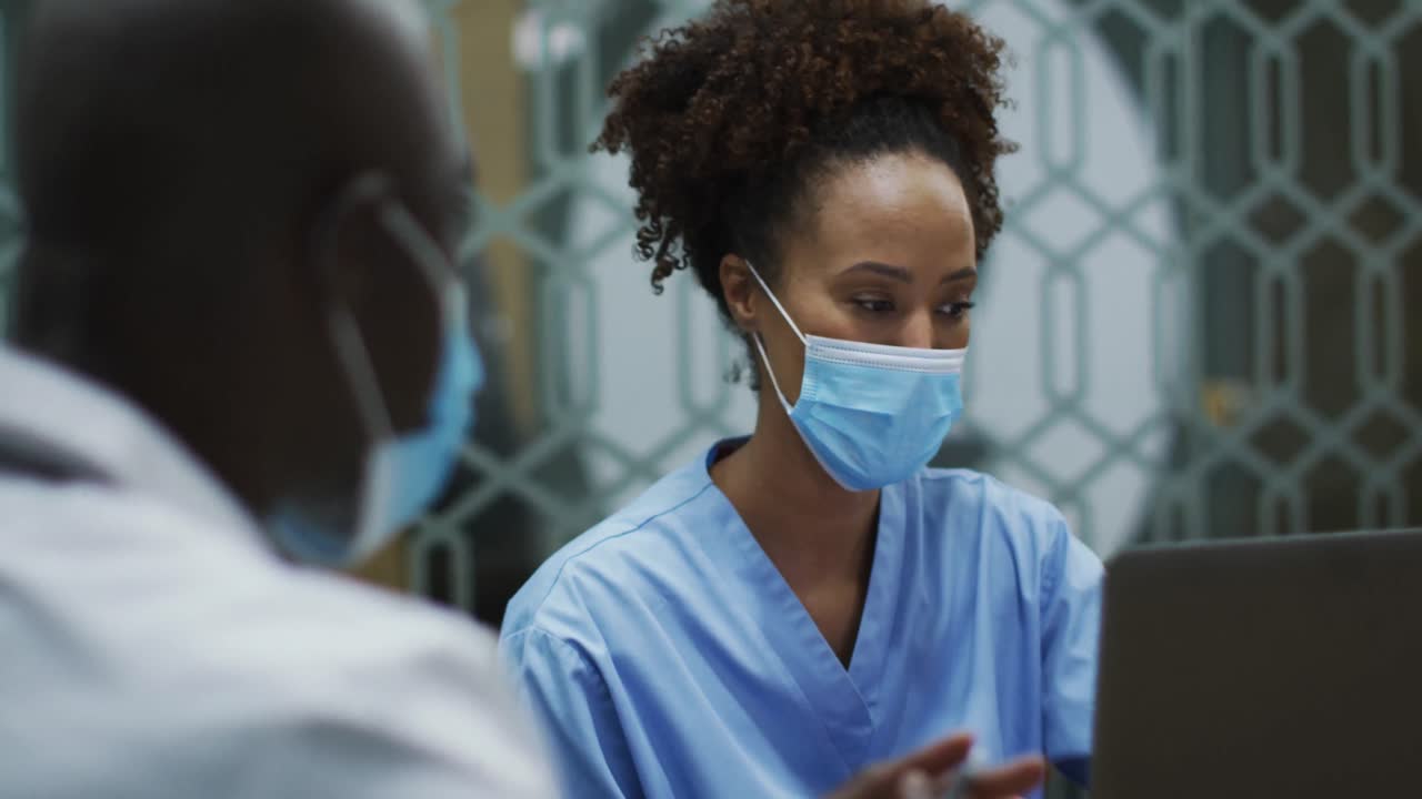 Medici uomini e donne di diverse etnie con mascherine discutono usando un laptop in ufficio.