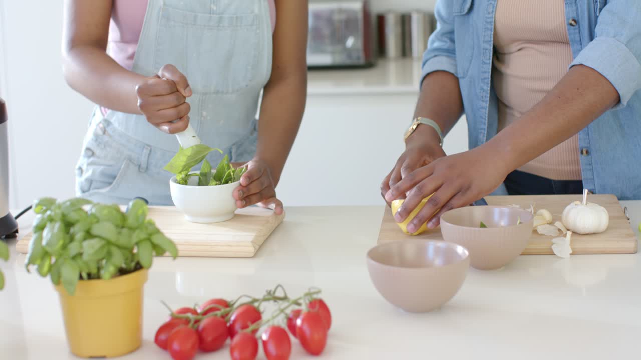 Giovani donne africane schiacciano basilico in una ciotola, mentre una donna taglia un limone e pela aglio sul bancone per un pasto.