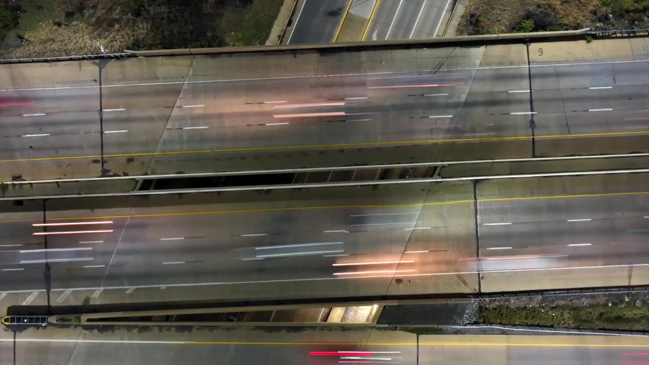 Ripresa aerea dall'alto di una scena di traffico in autostrada di notte. Fari bianchi e luci posteriori rosse di auto su un ponte. Hyperlapse di drone in discesa. Vista dall'alto. Scena di periferia urbana in America