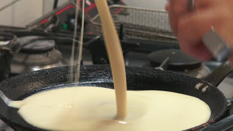 foto de un cocinero vertiendo masa en una sartén para hacer panqueques en una estufa