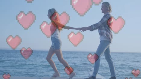 multiple red heart icons floating against caucasian couple holding hands walking near the sea